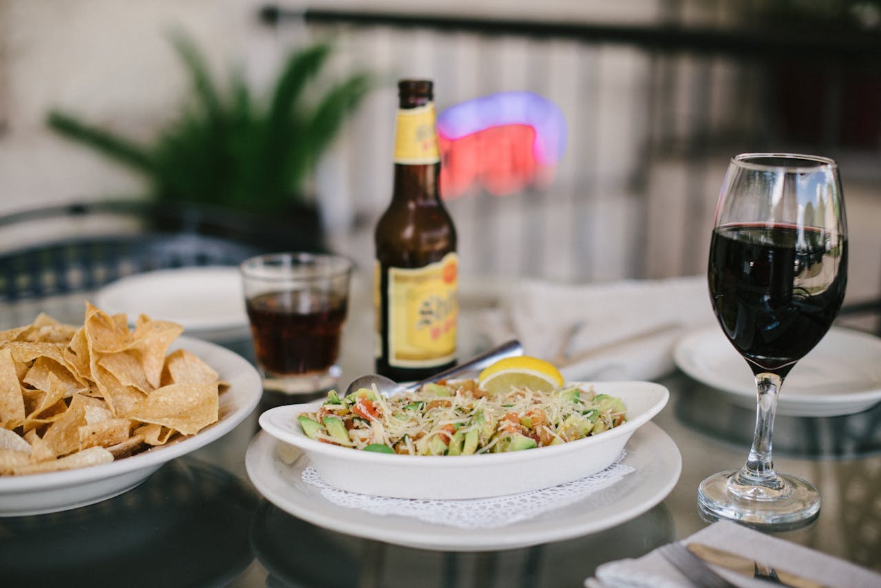 An inviting dining setup featuring tacos, chips, beer, and wine on a glass table in a relaxed indoor setting.